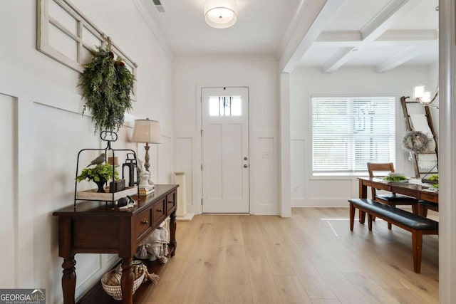 foyer with ornamental molding, beamed ceiling, light wood-style floors, a decorative wall, and wainscoting