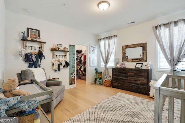 bedroom featuring a spacious closet, multiple windows, light wood finished floors, and a closet