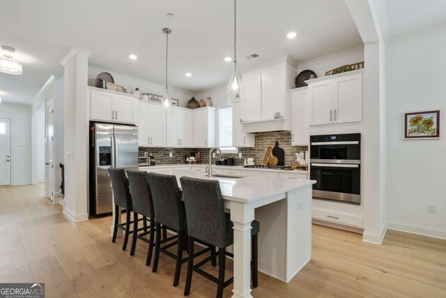 kitchen with backsplash, appliances with stainless steel finishes, an island with sink, and a sink
