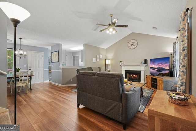 living room featuring a warm lit fireplace, wood finished floors, a textured ceiling, and ceiling fan with notable chandelier