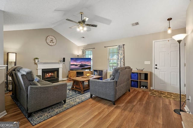 living room with visible vents, a glass covered fireplace, lofted ceiling, wood finished floors, and ceiling fan