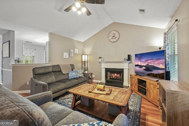 living area with vaulted ceiling, visible vents, light wood-style floors, ceiling fan, and a lit fireplace