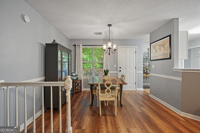 dining room with wood-type flooring, a textured ceiling, and an inviting chandelier