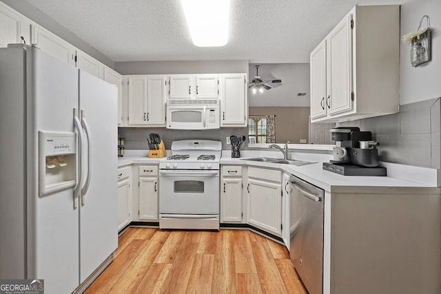 kitchen featuring white cabinets, light countertops, a sink, white appliances, and light wood-style floors