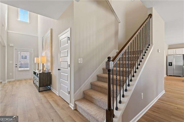 stairs with baseboards, wood finished floors, and a high ceiling