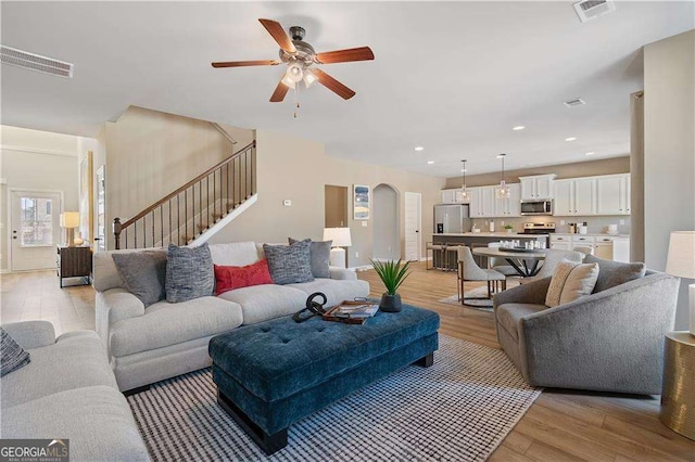 living room featuring stairway, ceiling fan, light wood finished floors, and visible vents
