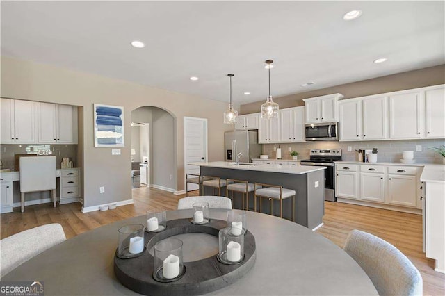 dining area with arched walkways, light wood-type flooring, baseboards, and recessed lighting