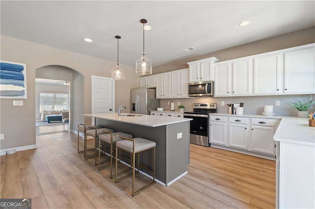 kitchen with stainless steel appliances, a kitchen breakfast bar, arched walkways, light wood-style floors, and decorative backsplash