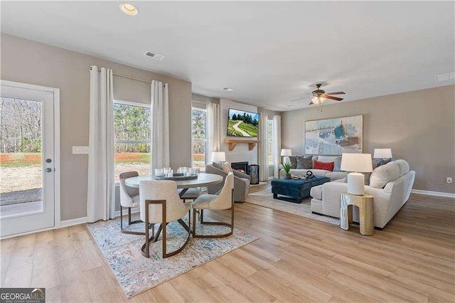 dining area with a ceiling fan, wood finished floors, a lit fireplace, baseboards, and visible vents