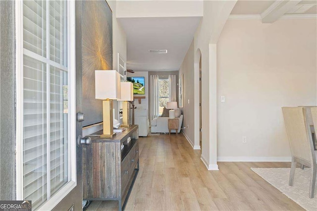 hallway featuring crown molding, light wood-type flooring, arched walkways, baseboards, and visible vents