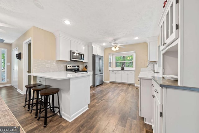 kitchen with white cabinets, appliances with stainless steel finishes, a ceiling fan, and a peninsula