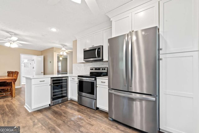kitchen featuring a ceiling fan, light countertops, a peninsula, appliances with stainless steel finishes, and wine cooler