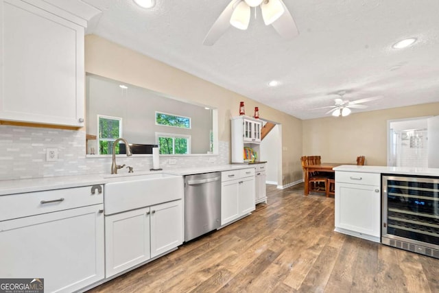 kitchen featuring stainless steel dishwasher, a ceiling fan, tasteful backsplash, beverage cooler, and white cabinets
