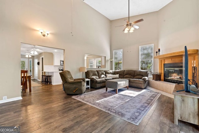 living area featuring dark wood-type flooring, a tile fireplace, a ceiling fan, and a towering ceiling