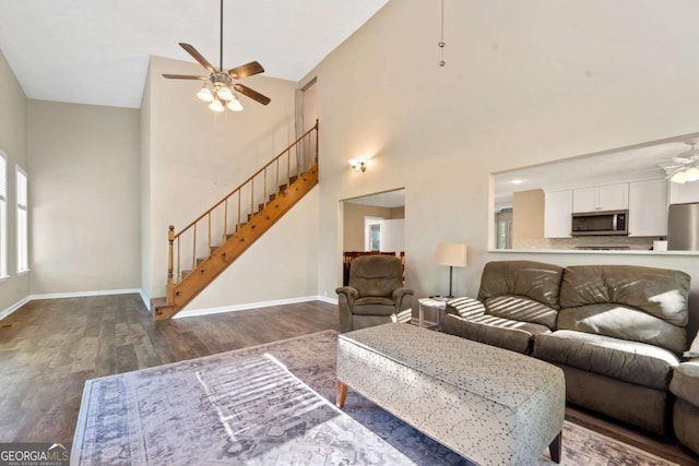 living room featuring stairway, high vaulted ceiling, a ceiling fan, wood finished floors, and baseboards