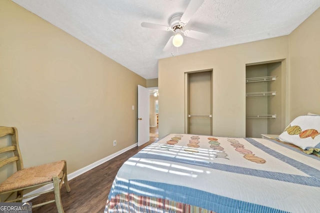 bedroom with a textured ceiling, baseboards, a ceiling fan, wood finished floors, and multiple closets