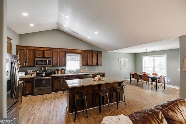 kitchen with a kitchen breakfast bar, dark brown cabinetry, light wood finished floors, appliances with stainless steel finishes, and a kitchen island