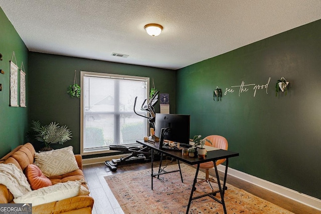 home office featuring a textured ceiling, wood finished floors, visible vents, and baseboards