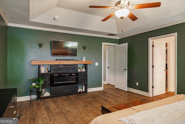 bedroom with baseboards, a glass covered fireplace, wood finished floors, crown molding, and a raised ceiling