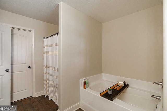 bathroom with curtained shower, a garden tub, wood finished floors, baseboards, and a textured ceiling