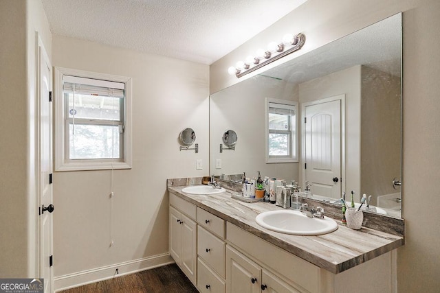 full bath with double vanity, a textured ceiling, wood finished floors, and a sink