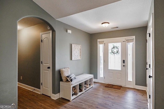 foyer with baseboards, wood finished floors, visible vents, and arched walkways