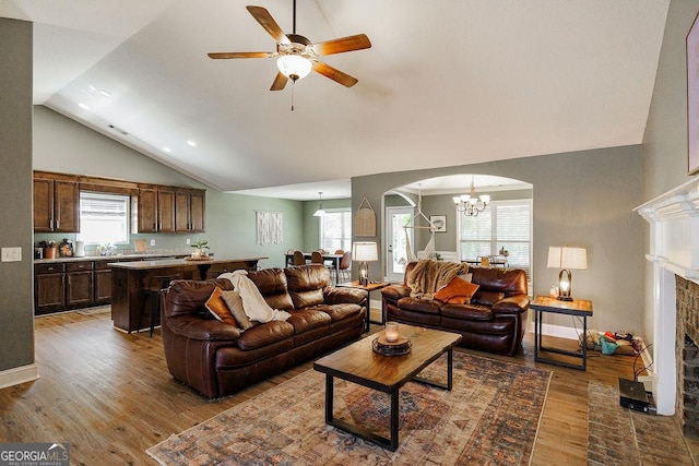 living room with wood finished floors, ceiling fan with notable chandelier, a wealth of natural light, arched walkways, and a fireplace