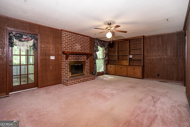 unfurnished living room with a fireplace, a ceiling fan, wooden walls, and carpet