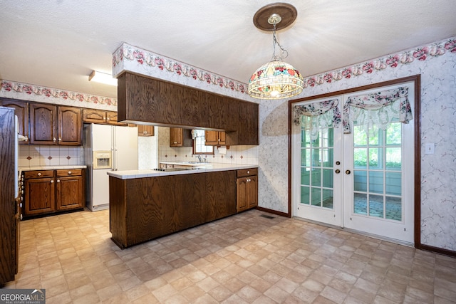 kitchen featuring a peninsula, wallpapered walls, light countertops, and white refrigerator with ice dispenser