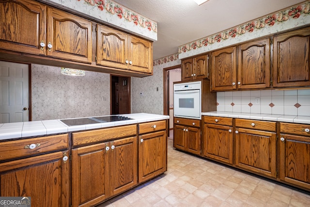 kitchen featuring white oven, wallpapered walls, tile counters, and light floors