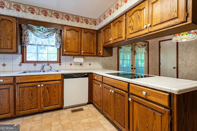 kitchen with a sink, a healthy amount of sunlight, wallpapered walls, black electric stovetop, and dishwasher