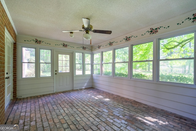 unfurnished sunroom with brick floor, a ceiling fan, and a textured ceiling