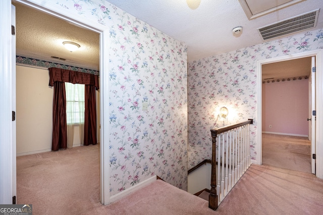interior space with carpet flooring, a textured ceiling, visible vents, an upstairs landing, and wallpapered walls