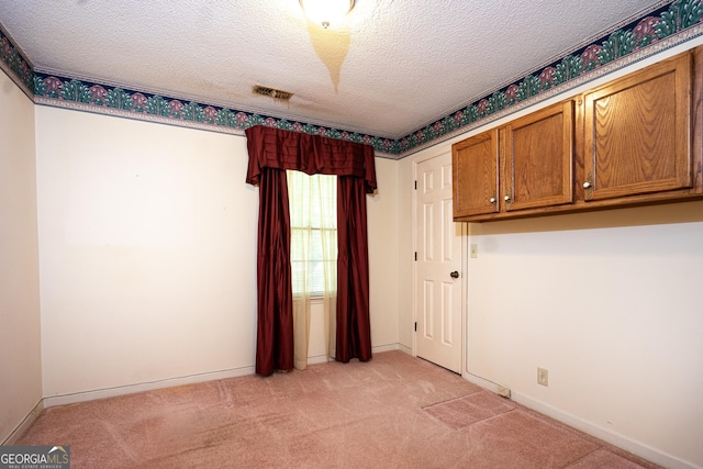 unfurnished room with light carpet, baseboards, visible vents, and a textured ceiling