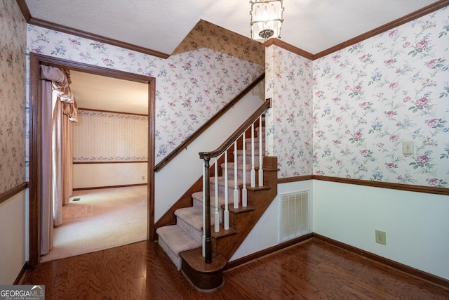 stairway with wallpapered walls, wood finished floors, visible vents, and crown molding