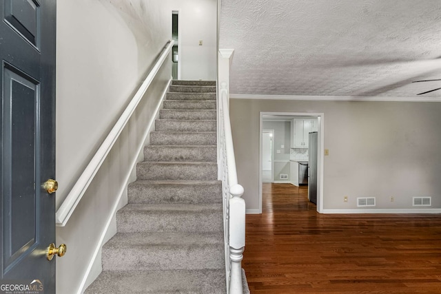 1320 Pinyon Pl, Lawrenceville, GA 30043 - stairs featuring crown molding, a textured ceiling, visible vents, and wood finished floors