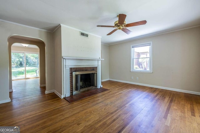unfurnished living room with arched walkways, wood finished floors, a ceiling fan, a brick fireplace, and baseboards
