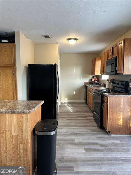 6630 Crystal Cove Trl, Gainesville, GA 30506 - kitchen with baseboards, light wood-style flooring, black appliances, brown cabinetry, and a textured ceiling