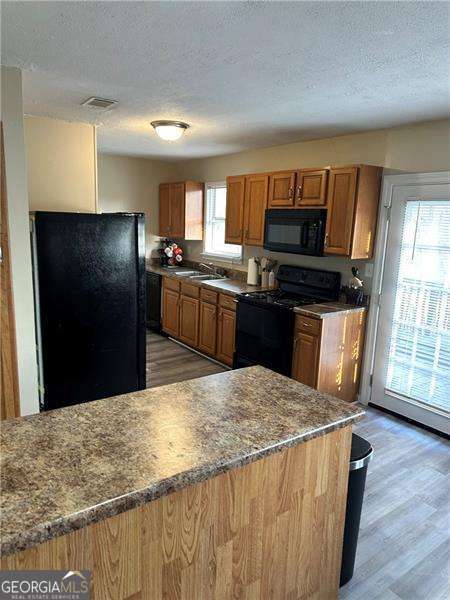 6630 Crystal Cove Trl, Gainesville, GA 30506 - kitchen featuring a textured ceiling, brown cabinetry, black appliances, light wood finished floors, and visible vents