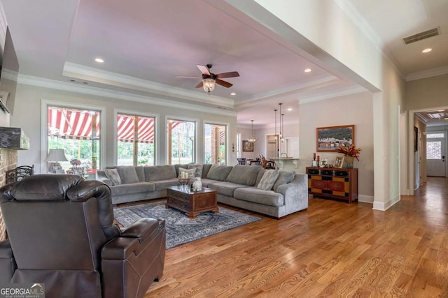 living area with a raised ceiling, a ceiling fan, visible vents, and light wood-type flooring