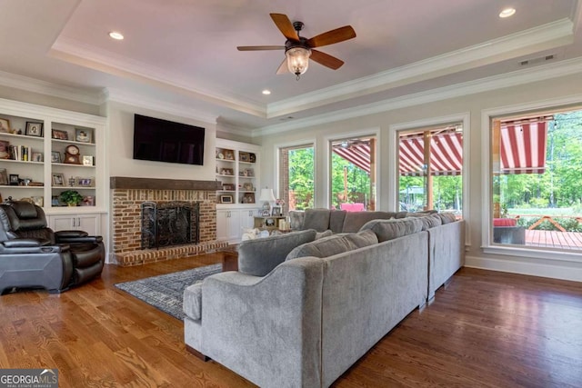 living room featuring a tray ceiling, plenty of natural light, a fireplace, and wood finished floors