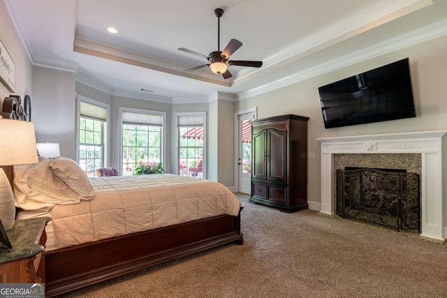 carpeted bedroom with a high end fireplace, ornamental molding, and a tray ceiling