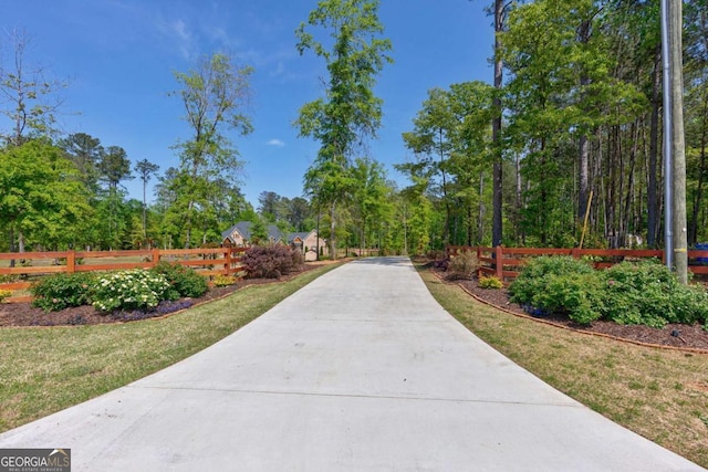view of property's community featuring concrete driveway, fence, and a lawn