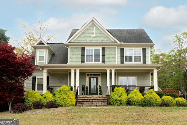view of front of house with a front lawn, a shingled roof, and covered porch
