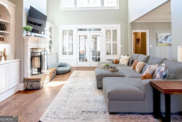 living room featuring ornamental molding, built in shelves, a high ceiling, and wood finished floors
