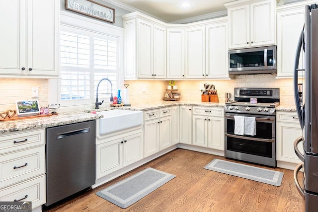 kitchen with a sink, appliances with stainless steel finishes, decorative backsplash, and light wood-type flooring