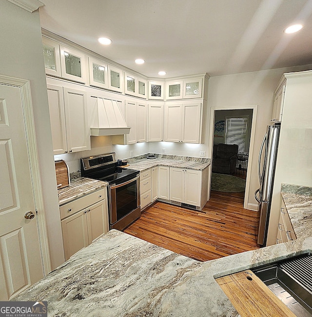 kitchen with dark wood-style flooring, custom exhaust hood, light stone countertops, white cabinets, and appliances with stainless steel finishes