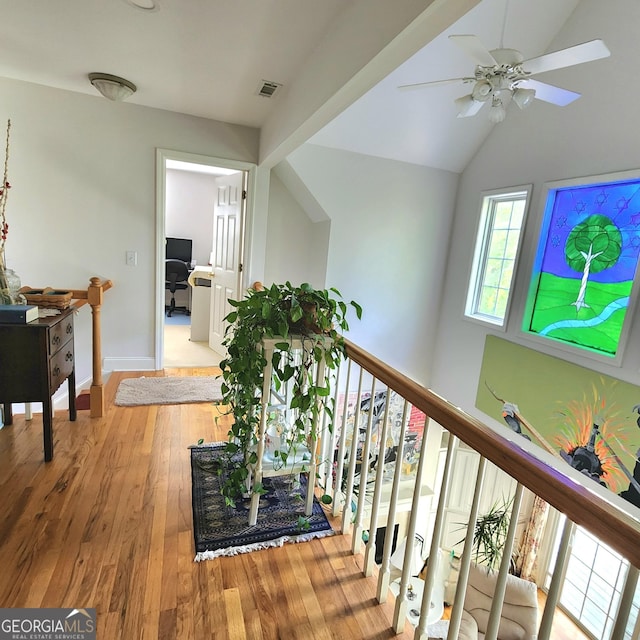hall featuring baseboards, visible vents, wood finished floors, and vaulted ceiling