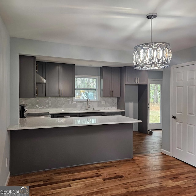 kitchen featuring a peninsula, a sink, tasteful backsplash, an inviting chandelier, and stove
