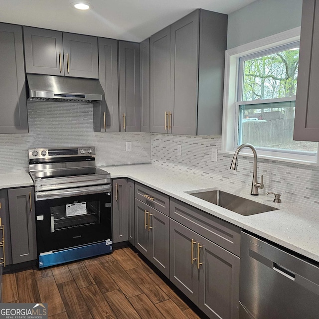 kitchen with stainless steel appliances, a sink, backsplash, gray cabinetry, and under cabinet range hood